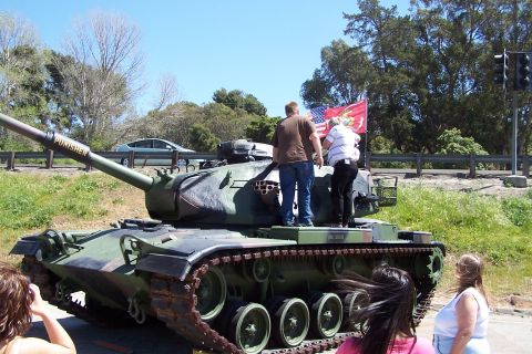 1990 Ford Bronco - A military tank with flags and people standing on it is parked outdoors on a sunny day.