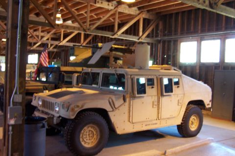 1990 Ford Bronco - A tan Humvee equipped with a weapon system is parked indoors next to another military vehicle.