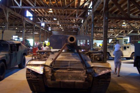1990 Ford Bronco - A tank sits in a large workshop with other military vehicles visible in the background.