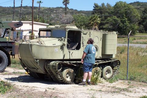 1990 Ford Bronco - A man inspects an olive drab tracked vehicle parked outdoors.