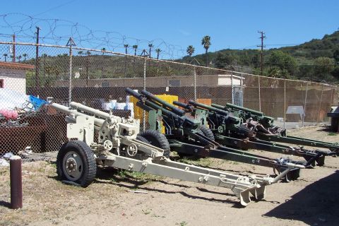 1990 Ford Bronco - Several artillery cannons are parked in a row outdoors, with a fence and buildings in the background.
