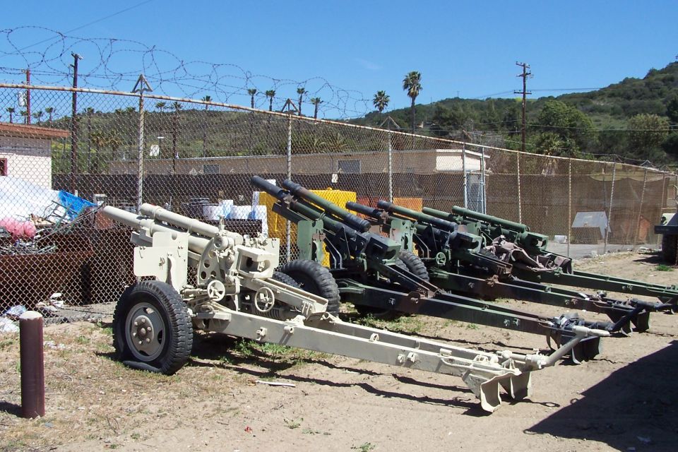 Artillery cannons lined up behind a chain-link fence with barbed wire