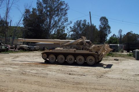 1990 Ford Bronco - Military self-propelled howitzer with a large cannon and tracked wheels sits in an outdoor storage area.