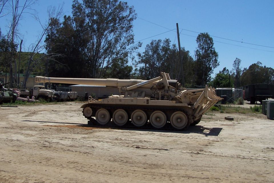Self-propelled howitzer with a long barrel and tracked chassis parked in a lot with other vehicles