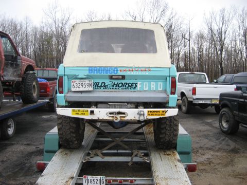 1991 Ford Bronco - A teal Ford Bronco with a soft top is loaded onto a trailer, parked with other vehicles.