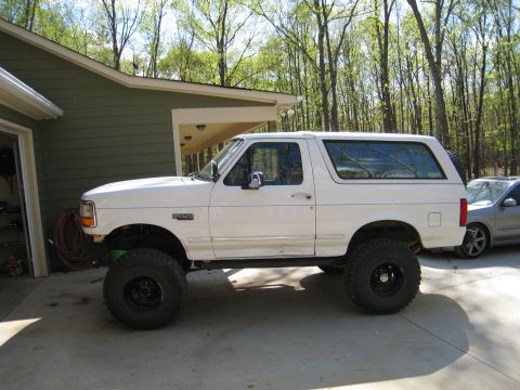 1996 Ford Bronco - Side view of a white 1996 Ford Bronco with large off-road tires and lifted suspension.