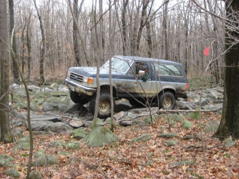 1991 Ford Bronco - A Ford Bronco navigates a rocky trail through a forest during an off-road event.