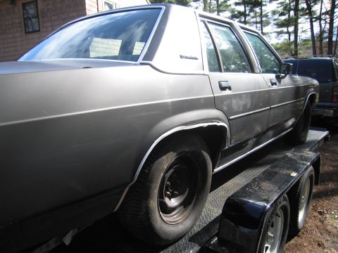 1991 Ford LTD Crown Victoria - Gray 1980s Ford sedan being transported on a trailer, with a dark SUV in the background.