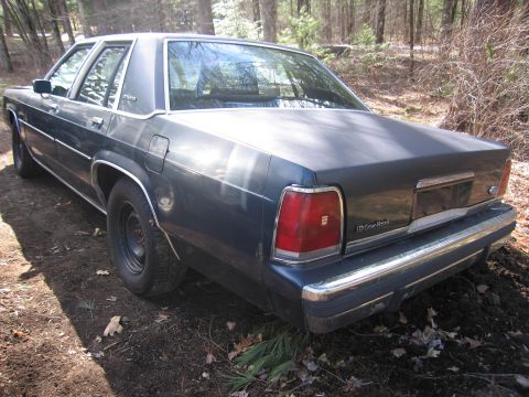 1991 Ford LTD Crown Victoria - Rear view of a dark blue 1990 Ford Crown Victoria LTD parked on a dirt road in a wooded area.