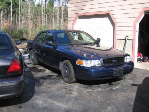 1991 Ford LTD Crown Victoria - A dark blue Ford Crown Victoria, likely a police interceptor model, is parked in front of a garage with another vehicle partially visible t…