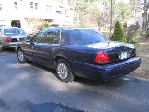 1991 Ford LTD Crown Victoria - Two sedans, possibly Ford Crown Victorias, parked in a driveway with a building and trees in the background.