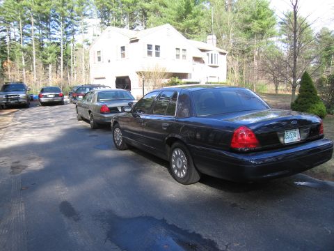 1991 Ford LTD Crown Victoria - Several cars are parked in a driveway in front of a house, with trees in the background.