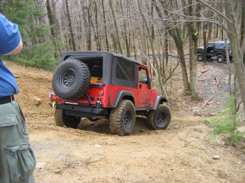 1991 Ford Bronco - A red Jeep Wrangler navigates a wooded trail with another vehicle visible in the background.