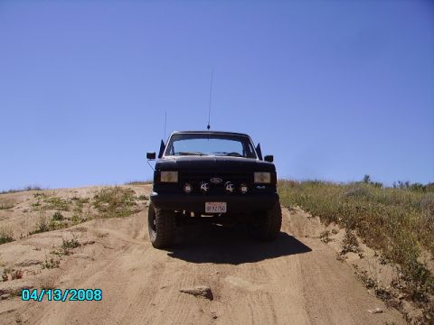 1990 Ford Bronco - A black Ford F-150 is shown driving up a sandy incline under a clear blue sky.