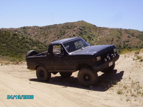 1990 Ford Bronco - A black Ford Bronco is seen off-roading on a sunny day.