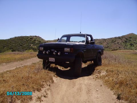 1990 Ford Bronco - A black Ford F-150 pickup truck is parked on a dirt path in a dry, hilly landscape.