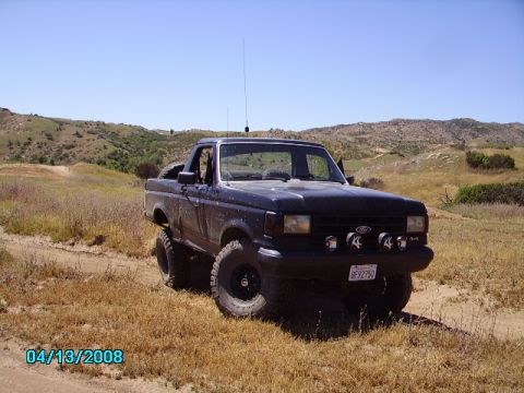 1990 Ford Bronco - This dark blue pickup truck features off-road modifications and is seen in a dry, hilly landscape.