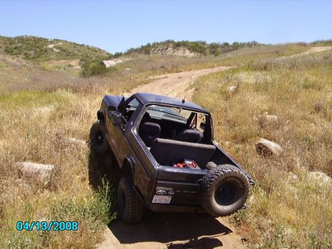1990 Ford Bronco - This dark blue Ford Bronco is seen off-roading on a dirt path with dry grass and hills in the background.