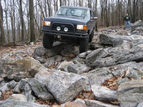1991 Ford Bronco - A Ford Bronco tackles a challenging rocky terrain in a wooded area.