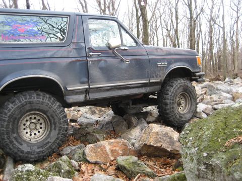 1991 Ford Bronco - A dark blue 1991 Ford Bronco is shown off-roading over a rocky trail.