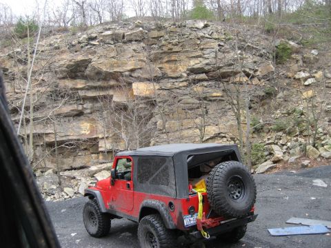 1991 Ford Bronco - Jeep Wrangler parked near a rocky cliff face, ready for off-road adventure.
