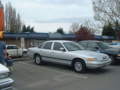 1987 Ford Crown Victoria LTD - A silver sedan is parked in a lot next to other vehicles. The car's body style suggests a 1990s model year.