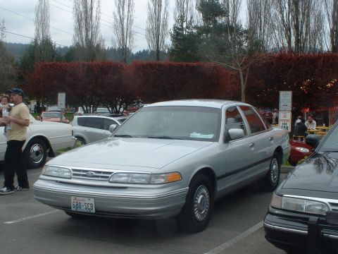 1987 Ford Crown Victoria LTD - A silver sedan is parked in a lot with other vehicles and trees in the background.
