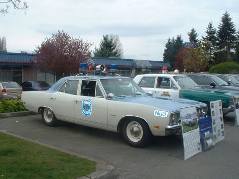 1987 Ford Crown Victoria LTD - A vintage police car, likely from the early 1970s, is displayed with informational boards at an outdoor event.