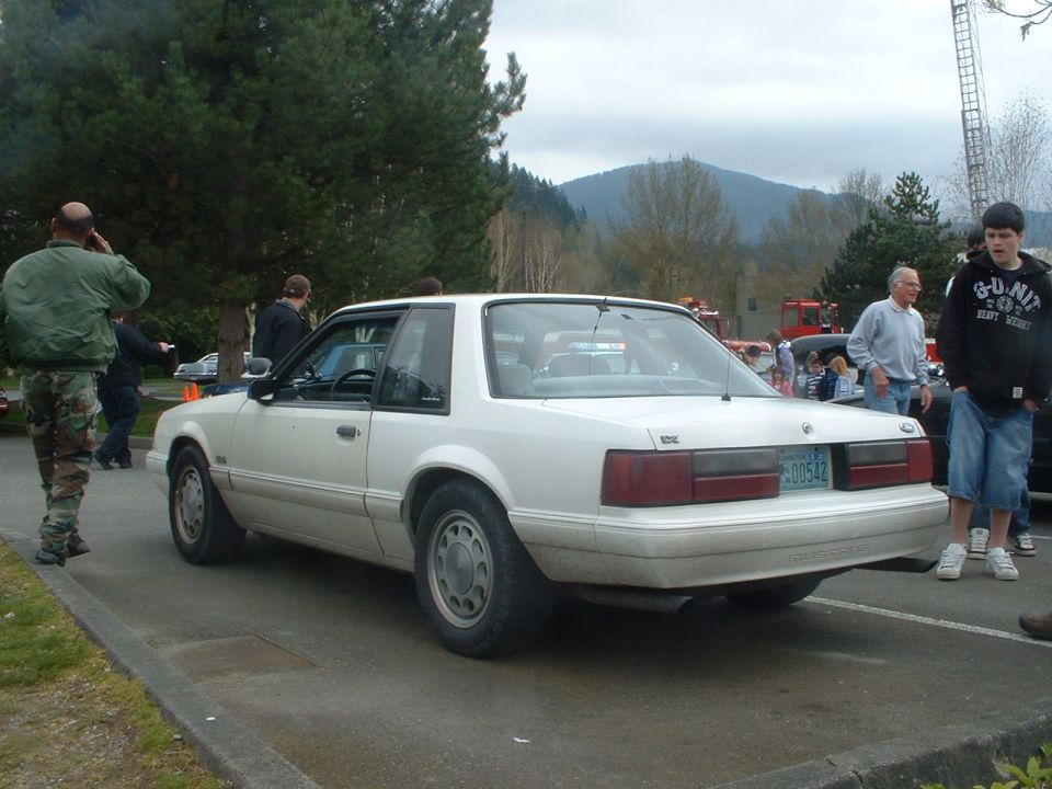 White coupe with a license plate reading 00542, seen from the rear