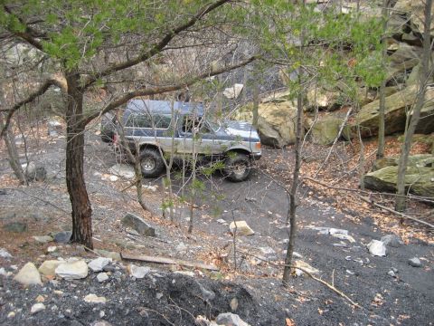 1991 Ford Bronco - A blue and silver 1991 Ford Bronco navigates a , wooded terrain during a meet and greet event.