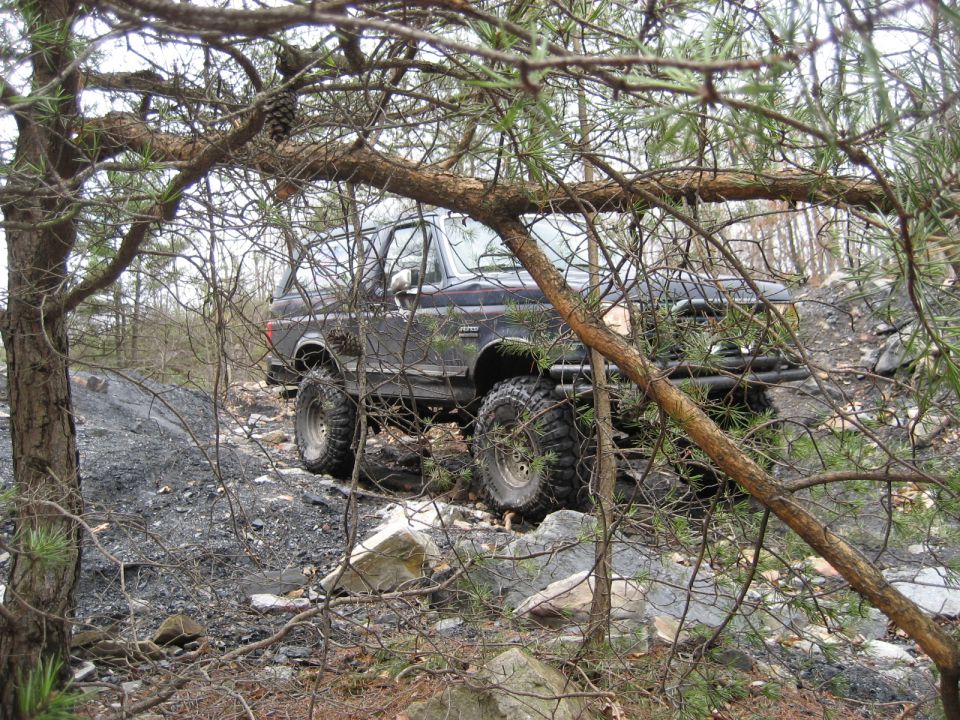 Dark Ford Bronco with large tires on a rocky, wooded trail