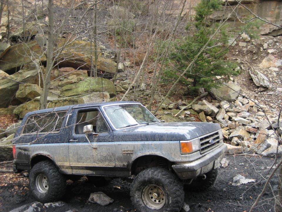 Mud-splattered blue and grey 1991 Ford Bronco on rocky terrain