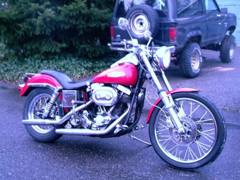 1972 Harley-Davidson Super Glide - A red 1972 Harley-Davidson Super Glide motorcycle is parked on a wet road, with a black SUV in the background.
