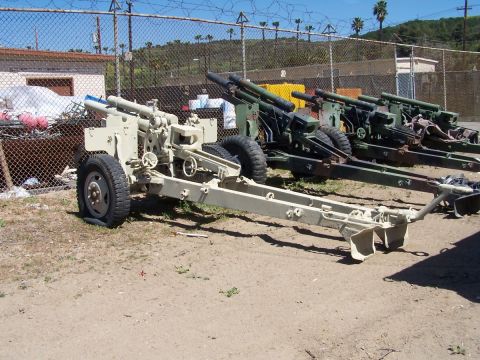 1990 Ford Bronco - Several artillery pieces are lined up outdoors, with a chain-link fence and buildings visible behind them.