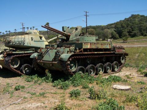1990 Ford Bronco - Two military tanks are parked outdoors in a field, one with a prominent double-barreled turret.