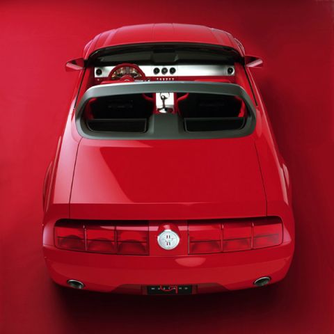 2005 Ford Mustang - Rear view of a red convertible sports car with its top down against a red background.
