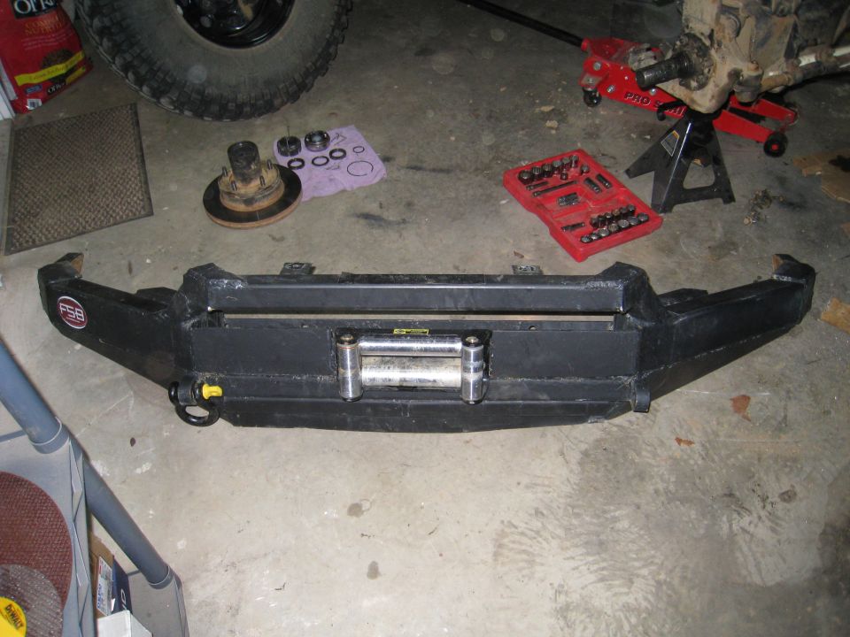 Black steel winch bumper with roller fairlead on garage floor beside hub and bearings