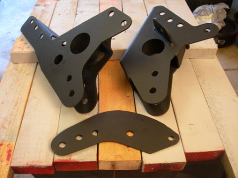 1985 Ford Bronco - These black metal suspension brackets are displayed on a wooden surface, with a website address visible at the bottom.