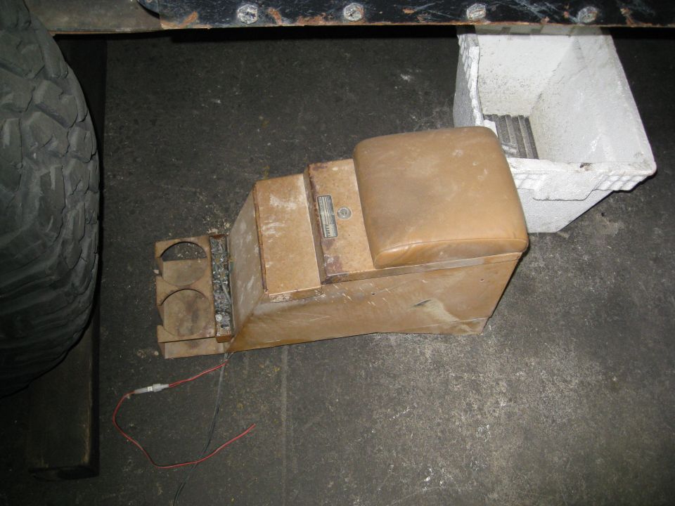 Tan center console with cup holders and armrest, next to a tire