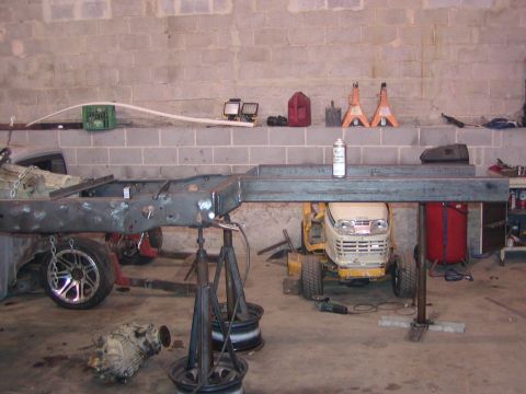 1991 Ford Bronco - The frame of a vehicle is elevated on stands, with a lawn tractor visible beneath it in a workshop setting.