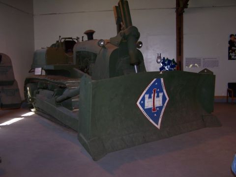 1990 Ford Bronco - Olive-drab military crawler bulldozer displayed indoors at a museum, its blade painted with the 1st Marine Division diamond insignia showin…