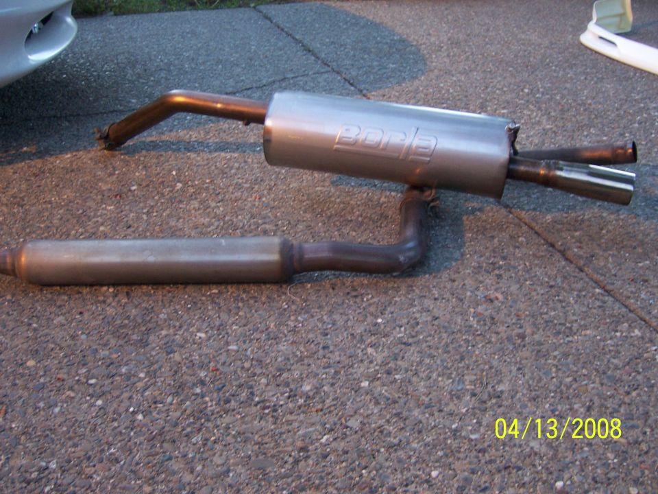 Borla exhaust system laid out on asphalt. A car fender is visible on the left