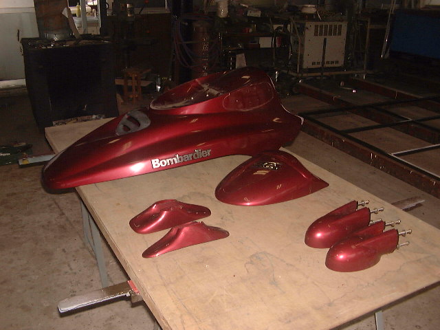 Red Bombardier personal watercraft body panels and hull section on a workbench