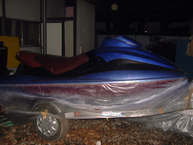 Blue jet ski with red seat on a trailer covered in plastic wrap