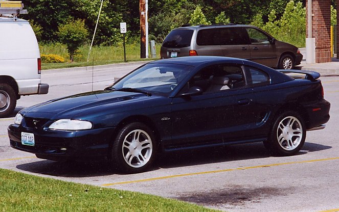 Dark green Ford Mustang GT coupe, front 3/4 view, in parking lot