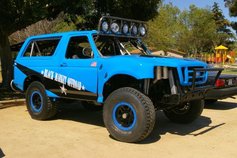 1986 Ford Bronco - Modified blue SUV with off-road tires and a prominent light bar on the roof.