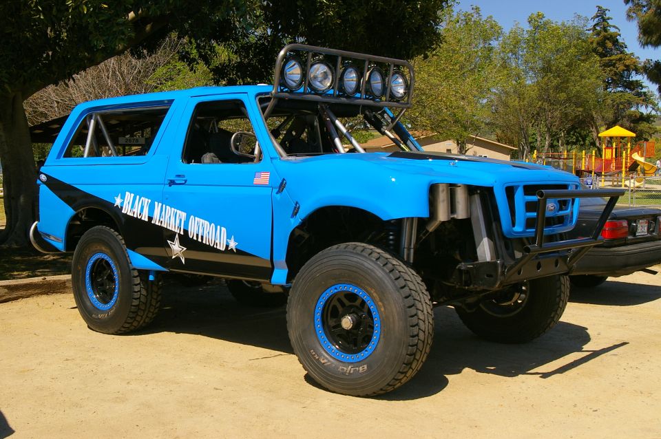 Blue off-road SUV with black stripe and "Black Market Offroad" text, roll cage, and light bar