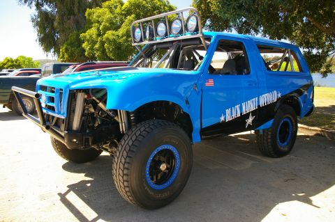 1986 Ford Bronco - Three-quarter front view of a bright blue full-size Ford prerunner SUV with a tube front bumper, exposed long-travel front suspension with…