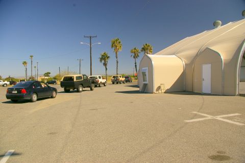 1986 Ford Bronco - A dark 1986 Ford Bronco with a camper shell is seen in a parking lot next to a large tent structure.