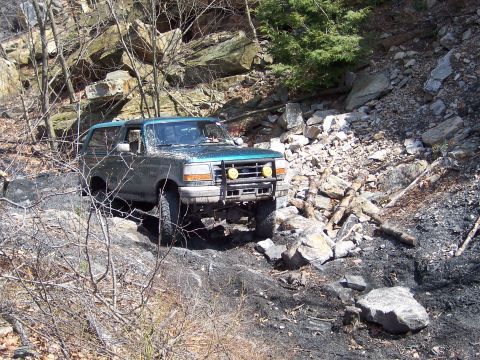 1996 Ford Bronco - A 1996 Ford Bronco navigates a rocky, off-road trail with steep, wooded slopes.
